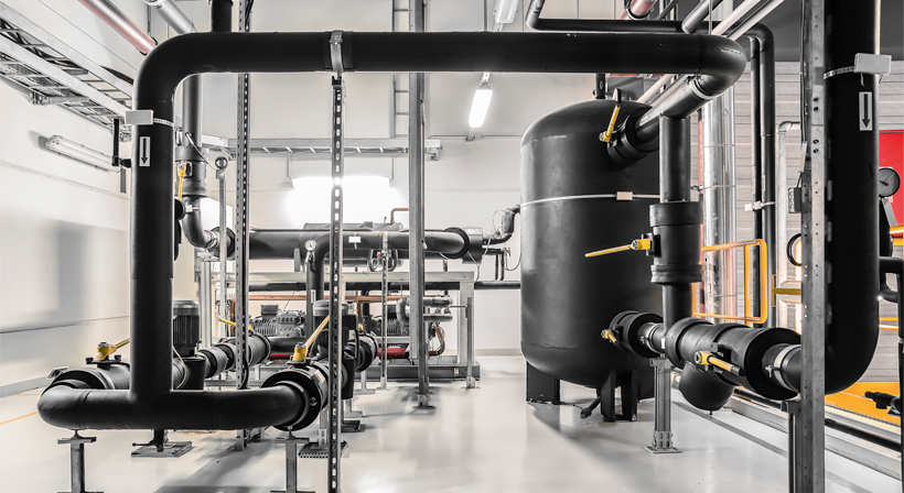 Thermally insulated pipework, valves and system tank in an industrial technical room for thermal insulation applications.