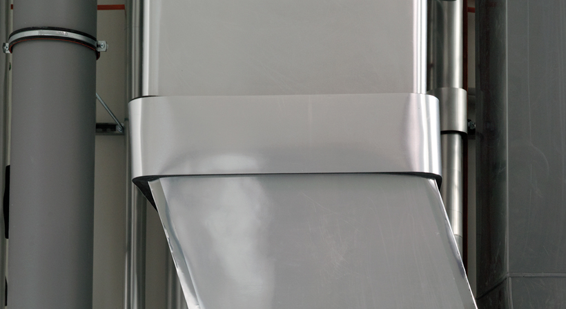 Close-up of a vertical duct with silver facing in a technical room.