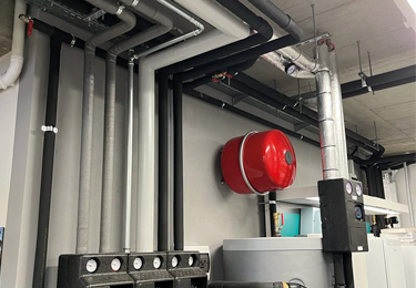 Insulated pipework installed along the ceiling and wall of a technical room.
