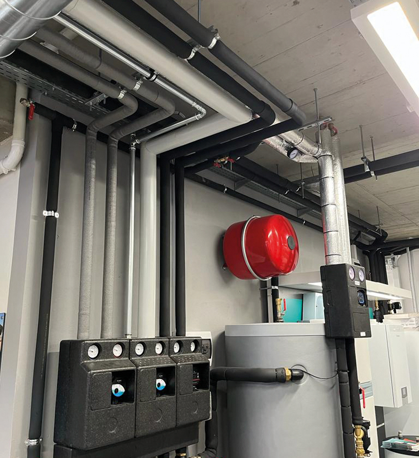 Vertical image of insulated black and grey pipes above mechanical control equipment.