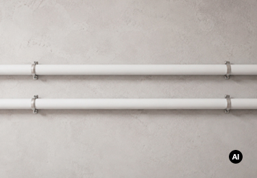 Two white multilayer pipes secured horizontally to a light concrete wall.