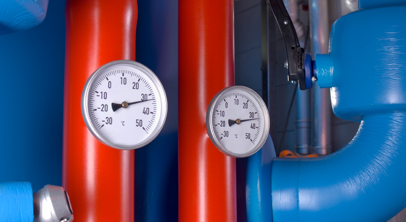 Temperature gauges on insulated red and blue pipes in a technical building system.