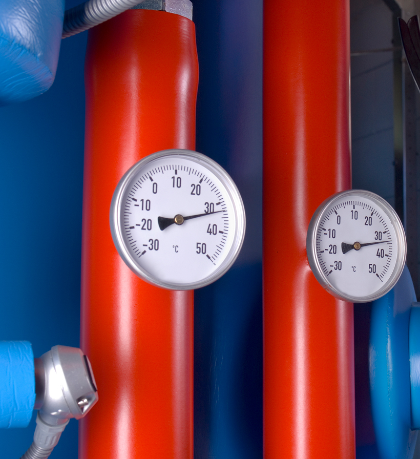 Two temperature gauges on red and blue insulated building-services pipes.