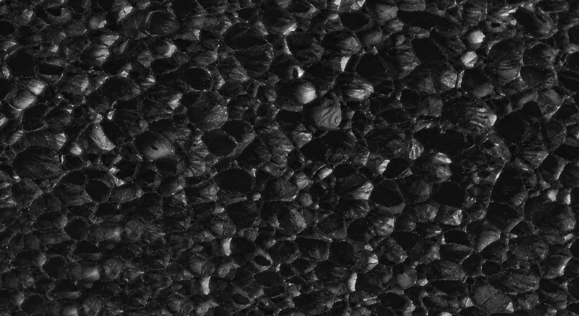 Macro view of a closed-cell material structure with small cavities on a yellow background.