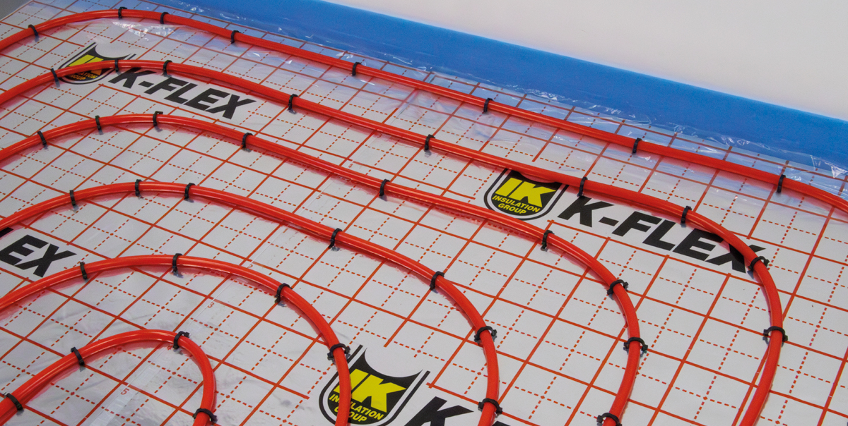 Red radiant heating pipes installed in curved loops over K-FLEX branded floor panels.