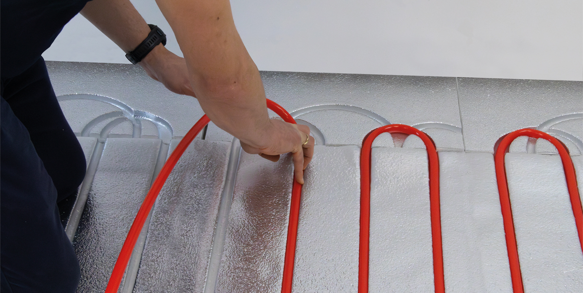 Installer presses a red multilayer pipe into routed underfloor heating panels.